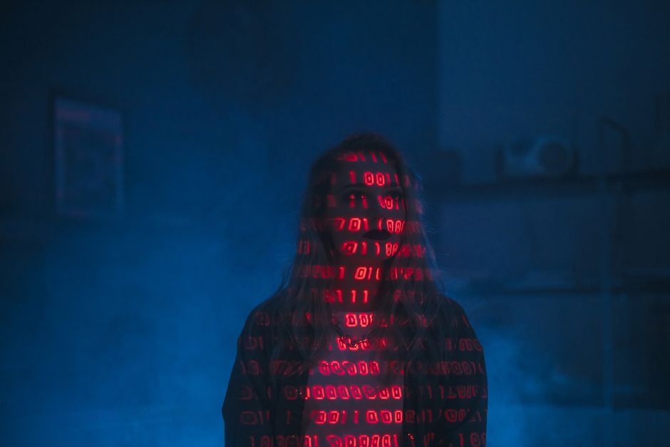 A close-up view of a computer monitor displaying lines of colorful programming code, with green, orange, and blue syntax highlighting on a black background. The text appears slightly blurred, focusing
